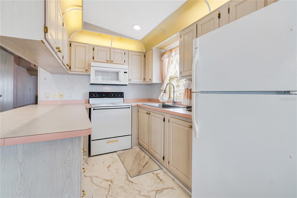 A kitchen features light wood cabinets, white appliances, pink-trimmed countertops, and a marble-patterned floor — 9000 US HIGHWAY 192 UNIT 517, CLERMONT, FL