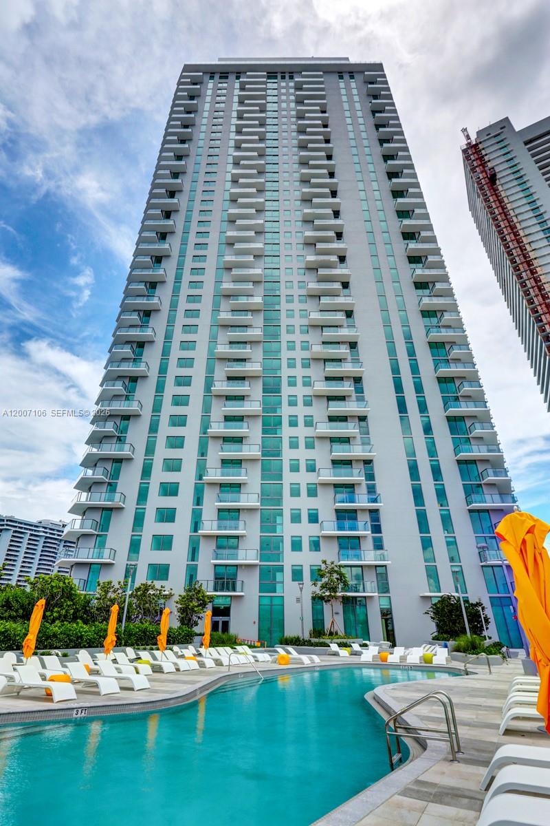 A tall residential high-rise building stands behind a swimming pool with lounge chairs — 501 NE 31st St # 910, Miami FL 33137, MIAMI, FL