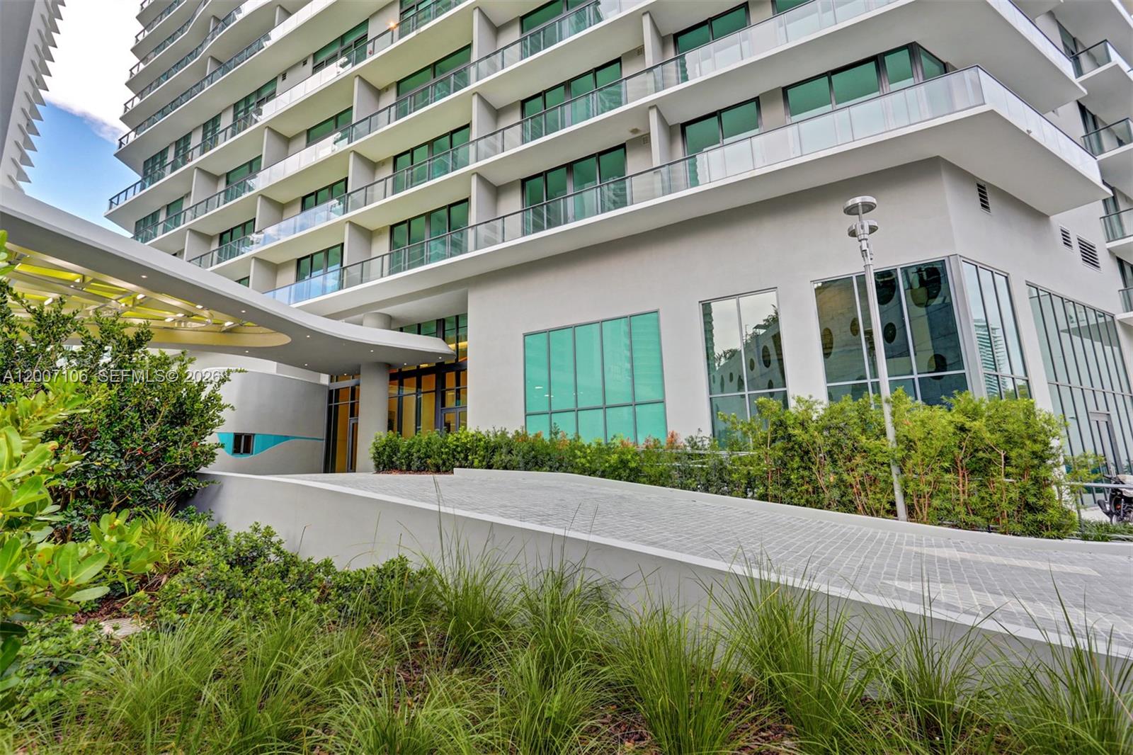 A modern high-rise building features a paved driveway ramp leading to a glass-fronted entrance — 501 NE 31st St # 910, Miami FL 33137, MIAMI, FL