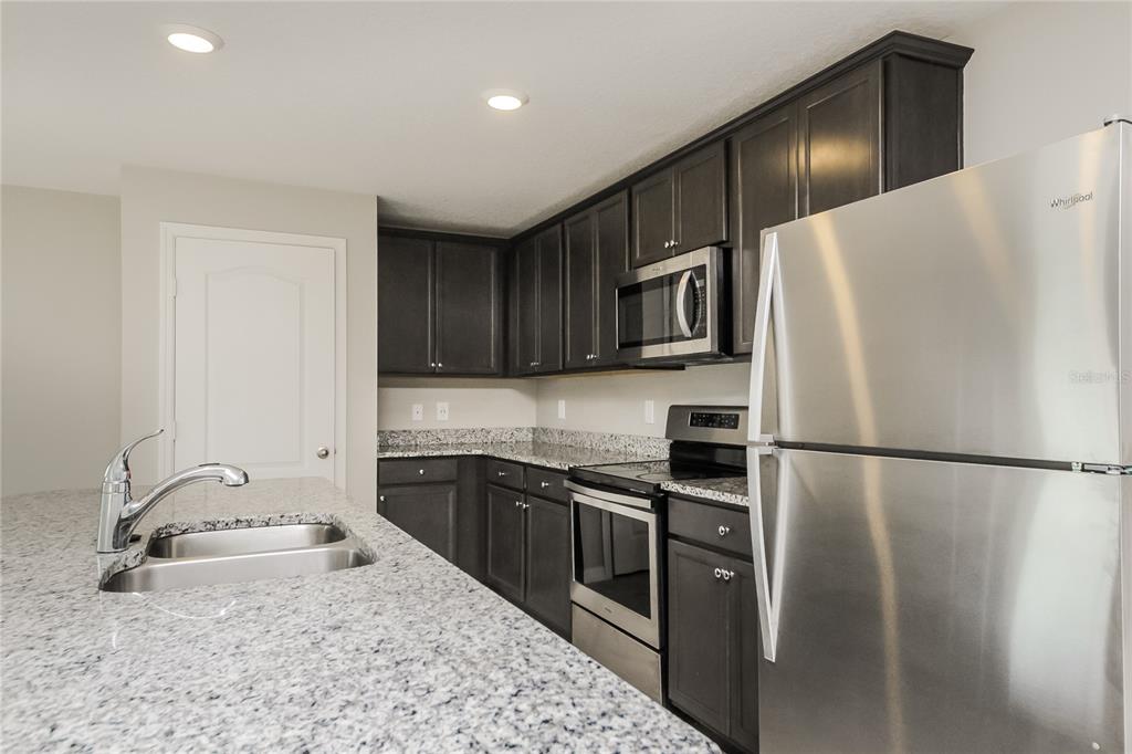 A kitchen features dark wood cabinets, granite countertops, and stainless steel appliances — 204 FIG COURT, KISSIMMEE, FL