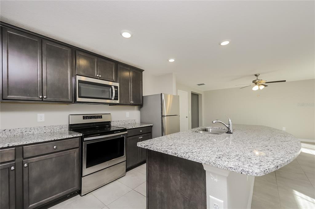 A kitchen features dark wood cabinets, granite countertops, stainless steel appliances, and a central island — 204 FIG COURT, KISSIMMEE, FL