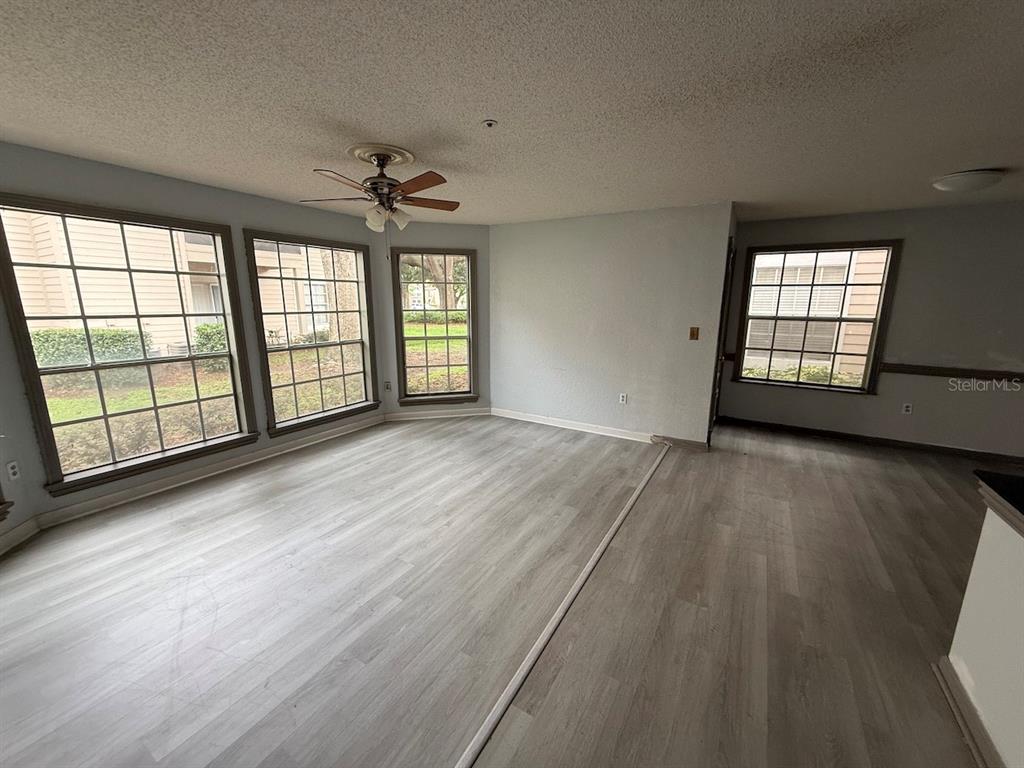 An empty living room features light wood-look flooring, a ceiling fan, and several large windows — 696 YOUNGSTOWN PARKWAY UNIT 315, ALTAMONTE SPRINGS, FL
