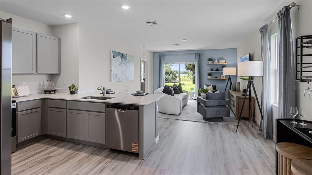 A modern kitchen with gray cabinets and a stainless dishwasher overlooks a furnished living area — 3316 WHITE INDIGO ROAD, WINTER HAVEN, FL