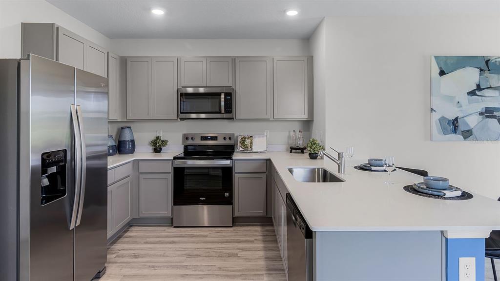 A modern kitchen features gray cabinets, stainless steel appliances, and a white quartz island countertop — 3316 WHITE INDIGO ROAD, WINTER HAVEN, FL