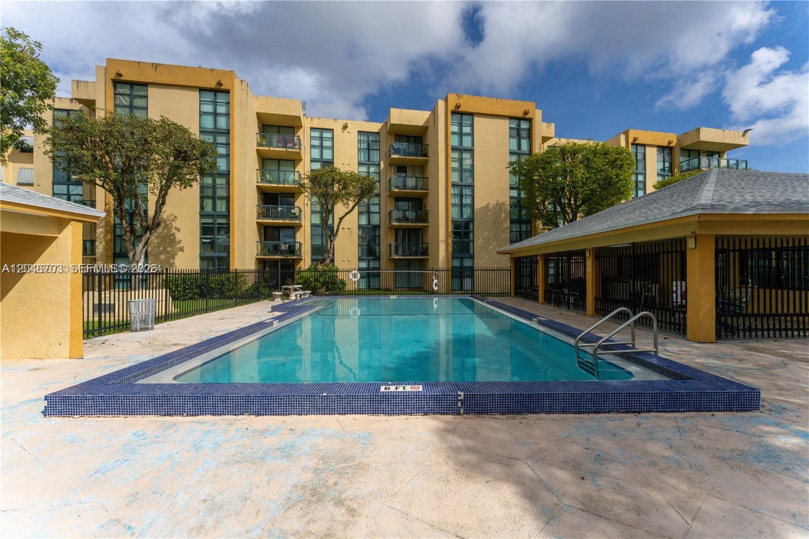 A rectangular swimming pool is situated in the courtyard of a multi-story yellow apartment building — 11780 SW 18th St # 2, Miami FL 33175, MIAMI, FL