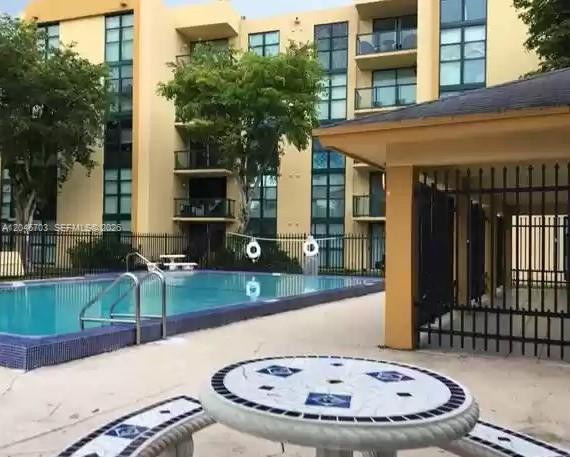 A swimming pool sits in front of a multi-story apartment building with a patio table — 11780 SW 18th St # 2, Miami FL 33175, MIAMI, FL