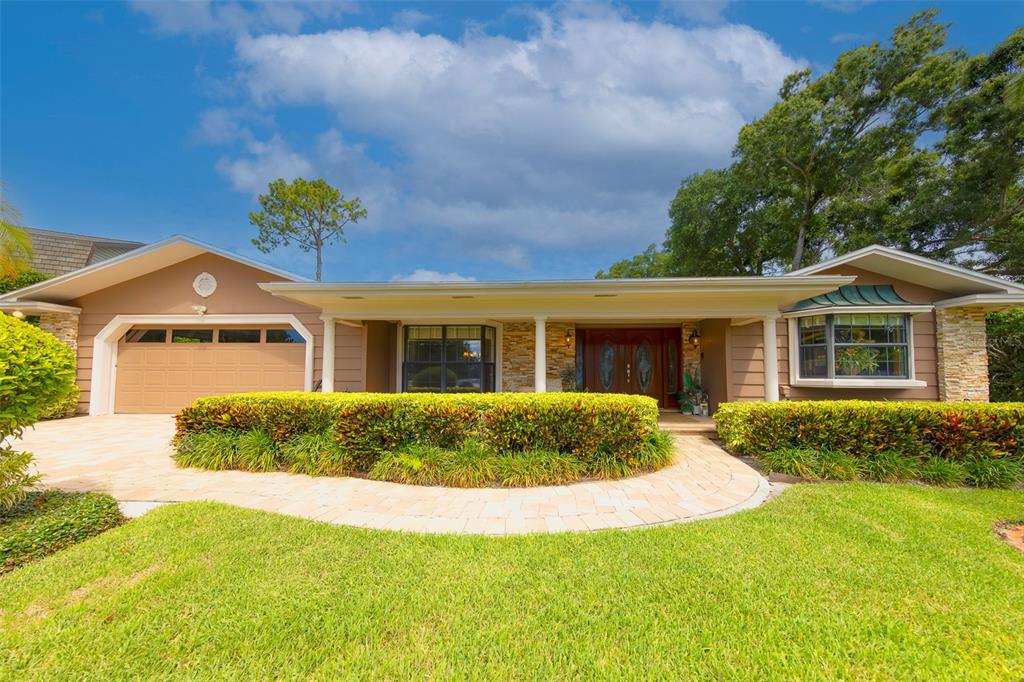 A single-story house with a tan exterior, stone accents, a garage, and a landscaped front yard — 2943 WHISPER LANE N, CLEARWATER, FL