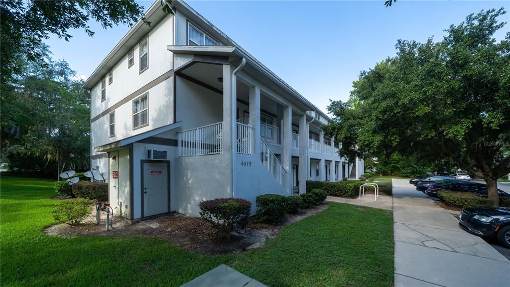 A multi-story apartment building exterior features a white facade, covered walkways, and a parking lot — 6519 W NEWBERRY RD UNIT A5, GAINESVILLE, FL