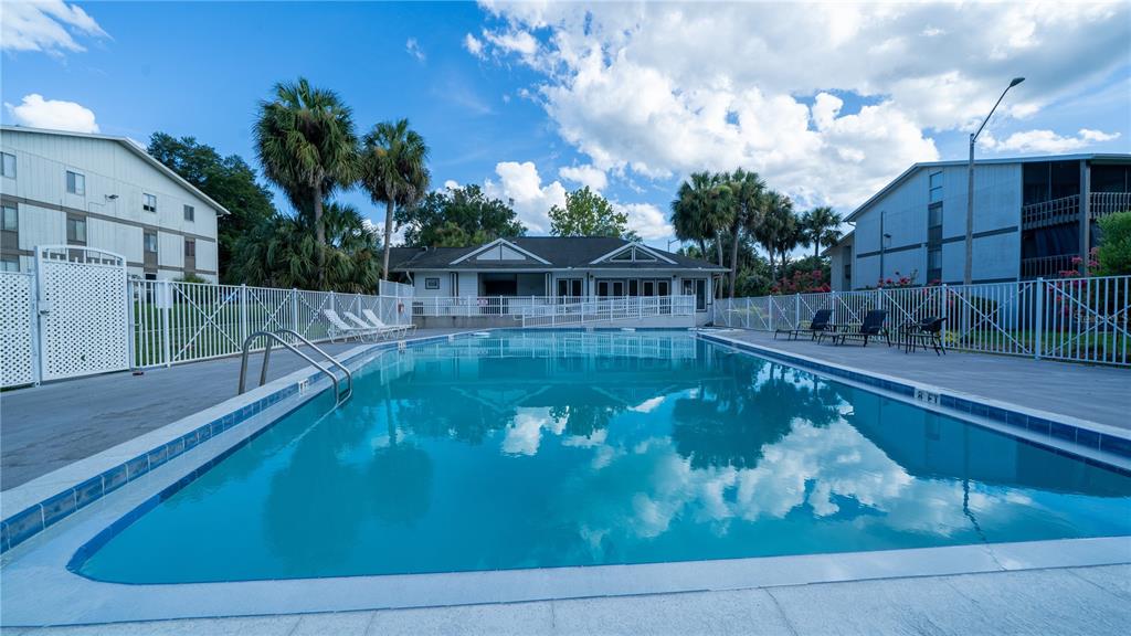 A rectangular outdoor swimming pool sits in front of a clubhouse with palm trees — 6519 W NEWBERRY RD UNIT A5, GAINESVILLE, FL