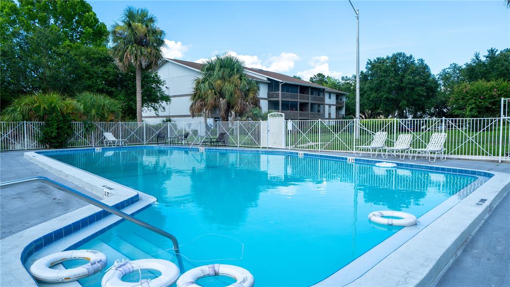 An outdoor swimming pool is surrounded by a white fence, lounge chairs, and palm trees — 6519 W NEWBERRY RD UNIT A5, GAINESVILLE, FL