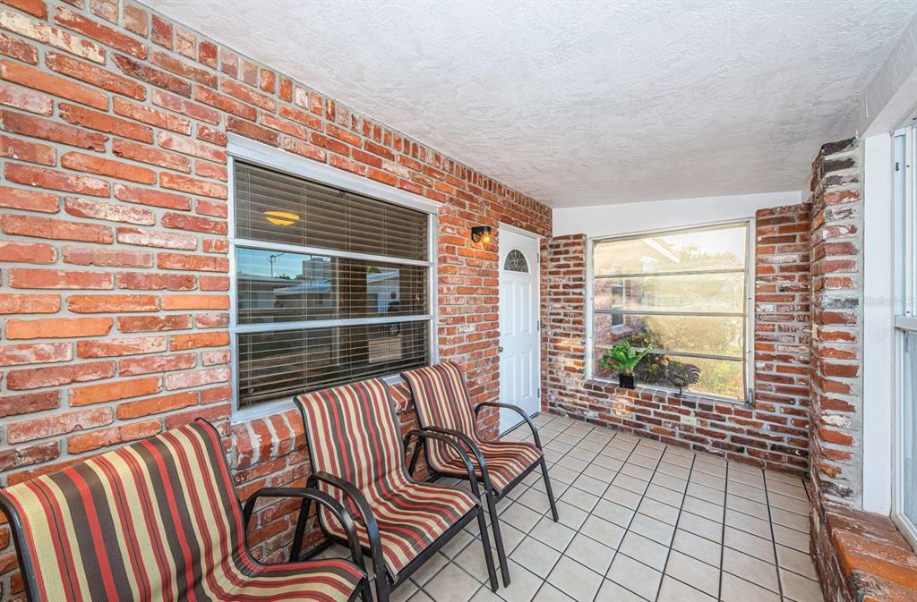 A covered porch features red brick walls, tiled flooring, and three striped outdoor chairs — 6020 MIDNIGHT PASS ROAD UNIT 40, SARASOTA, FL
