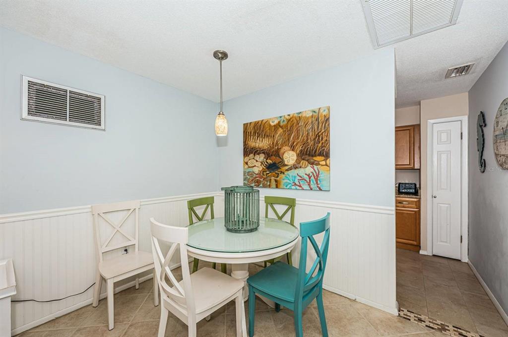 A dining area features a glass-topped table, mismatched chairs, and coastal artwork on light walls — 6020 MIDNIGHT PASS ROAD UNIT 40, SARASOTA, FL