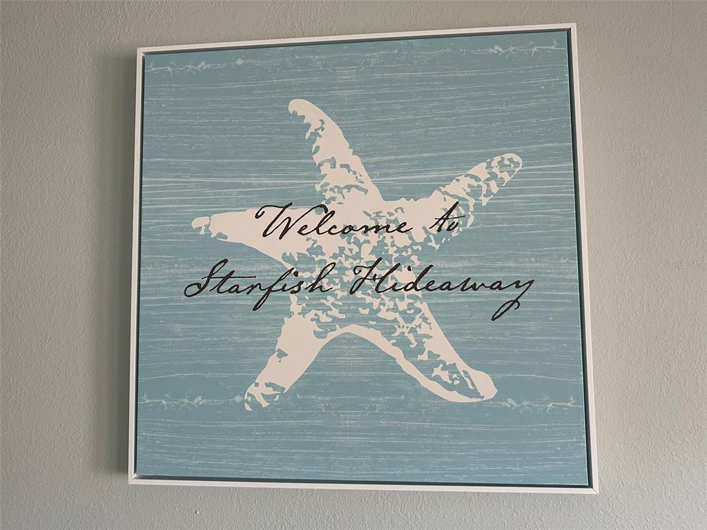 A square wall art piece featuring a starfish graphic and the text Welcome to Starfish Hideaway — 5006 STARFISH DR SE UNIT A, ST PETERSBURG, FL