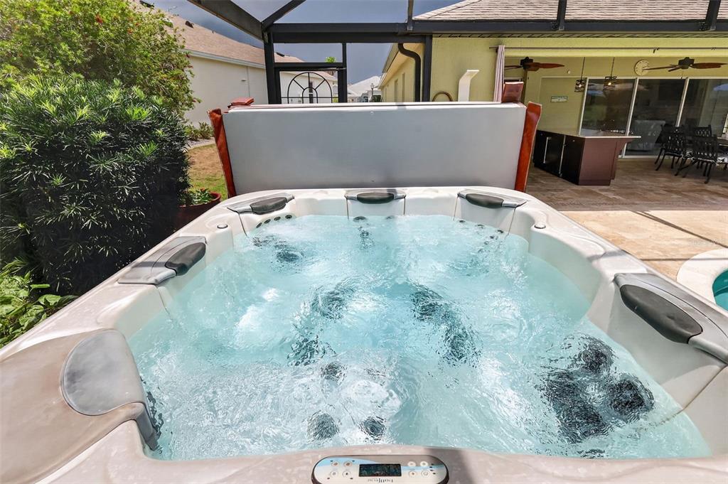 A hot tub with bubbling water sits on a patio inside a screened-in enclosure — 2773 DAY LILY RUN, THE VILLAGES, FL