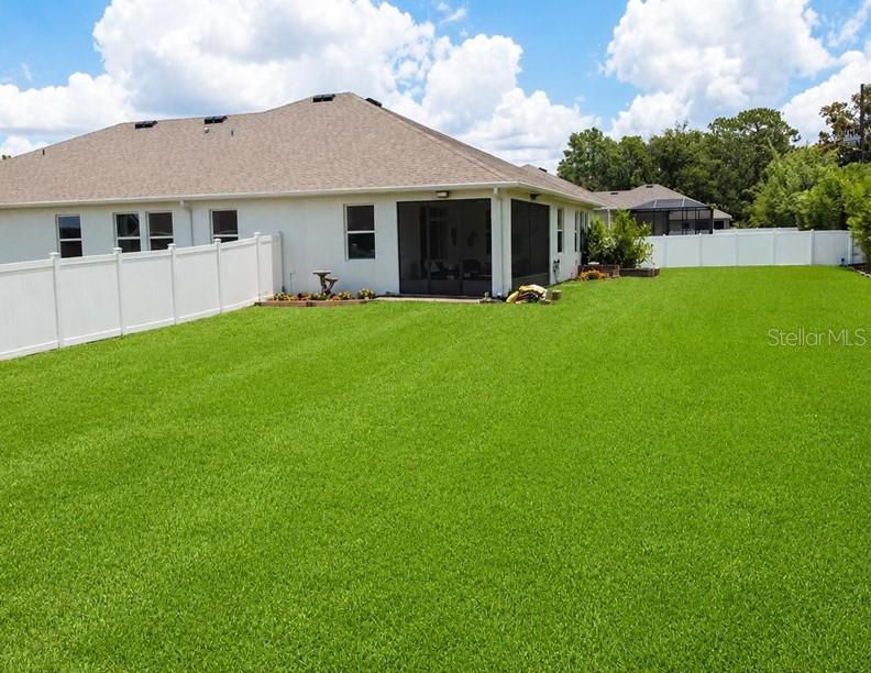 A backyard with a green lawn, a white vinyl fence, and a house with a lanai — 1340 SE 63RD COURT ROAD, OCALA, FL
