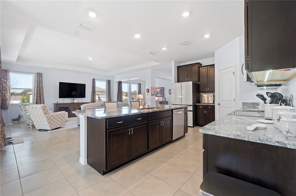 A kitchen with dark wood cabinets and granite countertops overlooks an open-concept living area — 1340 SE 63RD COURT ROAD, OCALA, FL