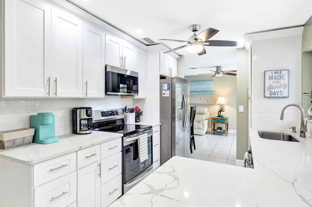 A white kitchen features marble-look countertops, stainless steel appliances, and a ceiling fan — 5103 PELICAN BOULEVARD, CAPE CORAL, FL