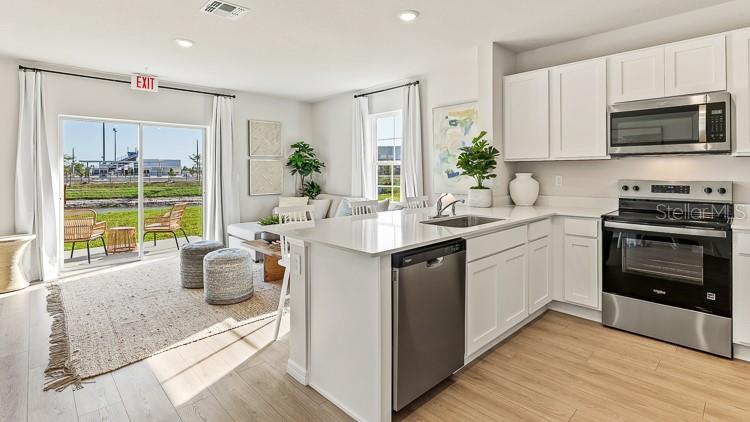 A modern kitchen with white cabinets and stainless steel appliances opens to a living area — 18643 BUCKSKIN DRIVE, LAKEWOOD RANCH, FL