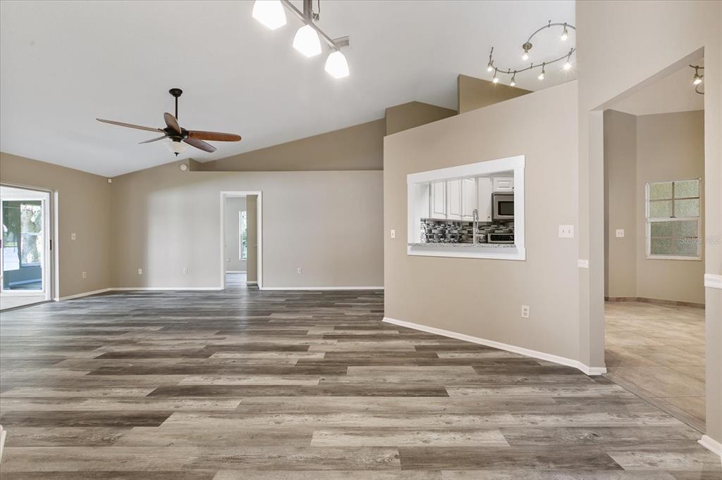 An open-concept living area features vaulted ceilings, wood-look flooring, and a kitchen pass-through window — 11647 FOX CREEK DRIVE, TAMPA, FL