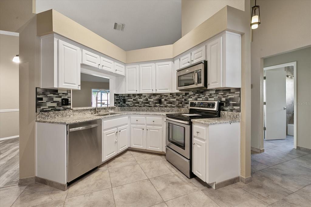 A kitchen with white cabinets, granite countertops, stainless steel appliances, and a tiled backsplash — 11647 FOX CREEK DRIVE, TAMPA, FL