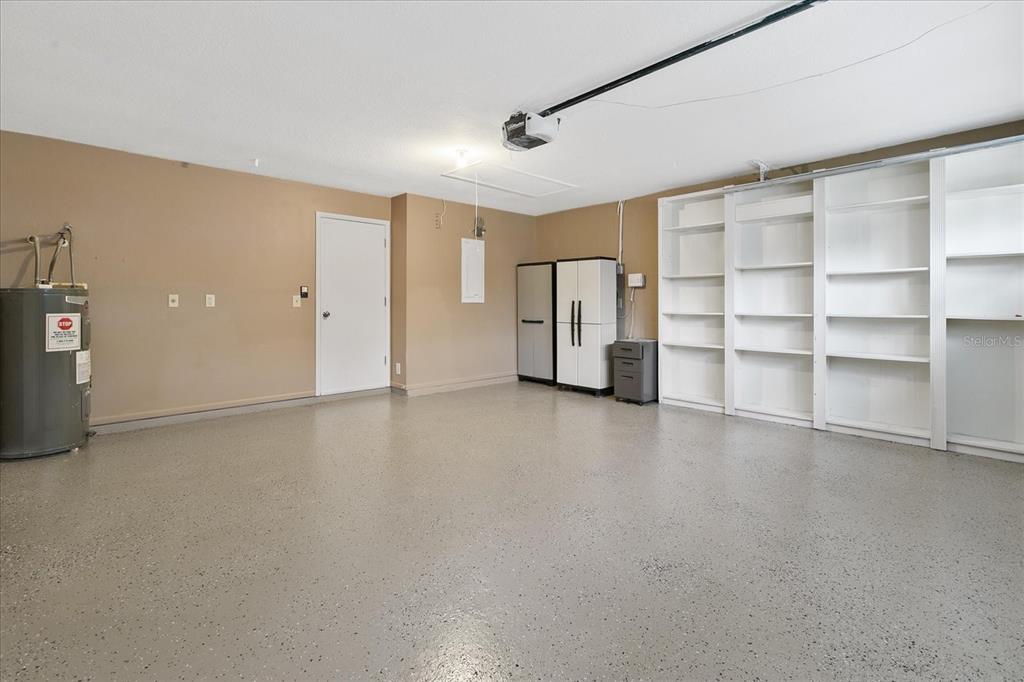 A garage with a speckled epoxy floor, built-in shelving, storage cabinets, and a water heater — 11647 FOX CREEK DRIVE, TAMPA, FL
