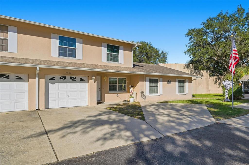 A two-story tan townhouse with a white garage door and a front concrete driveway — 7363 62ND AVENUE N, PINELLAS PARK, FL