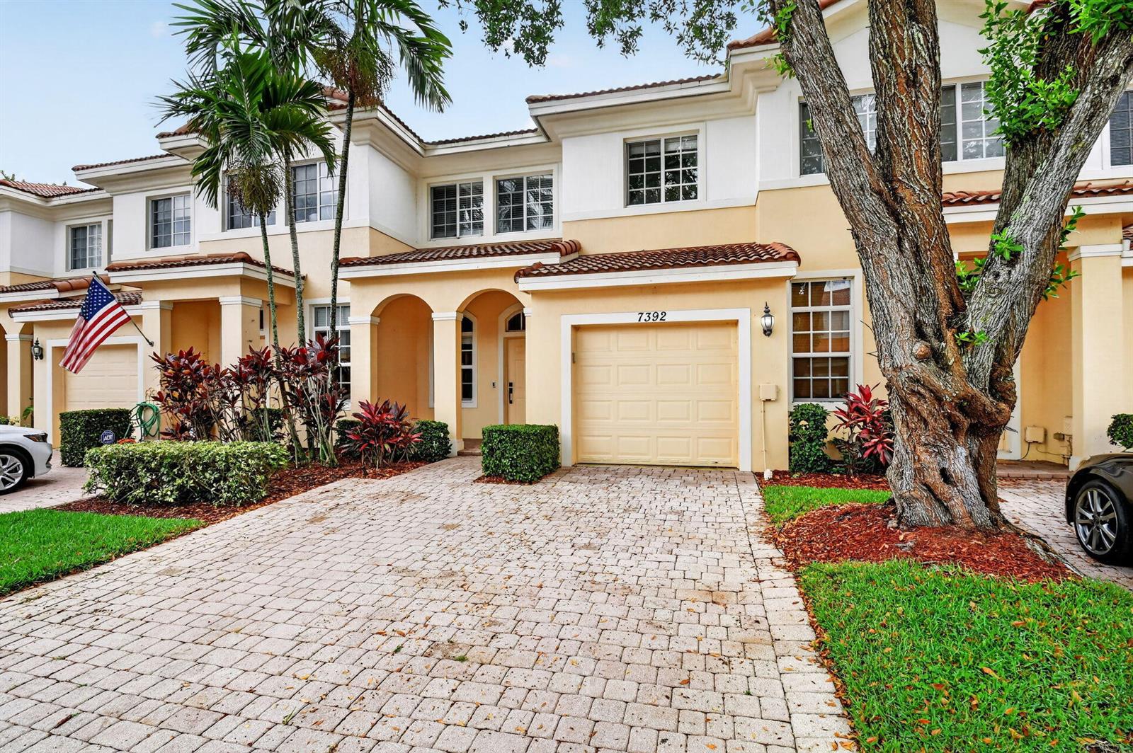 A two-story townhouse with a paved driveway, a one-car garage, and a large tree — 7392 Briella Drive, Boynton Beach FL 33437, BOYNTON BEACH, FL
