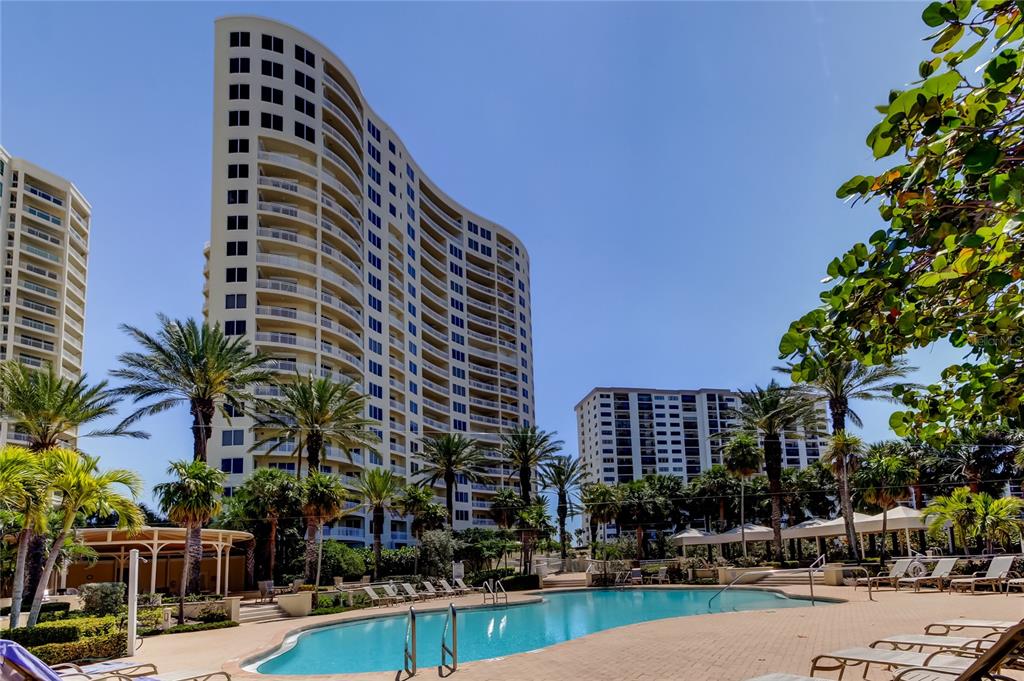 A swimming pool sits in front of two tall residential buildings surrounded by palm trees — 1200 GULF BOULEVARD UNIT 101, CLEARWATER BEACH, FL