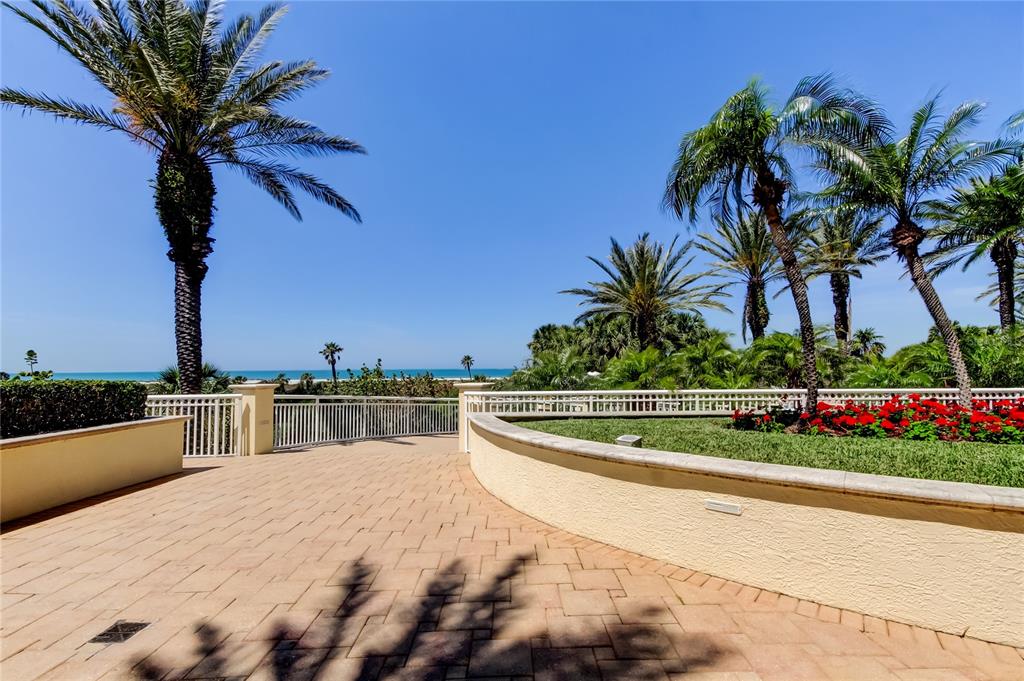 A paved patio overlooks a beach and ocean, framed by palm trees and landscaping — 1200 GULF BOULEVARD UNIT 101, CLEARWATER BEACH, FL