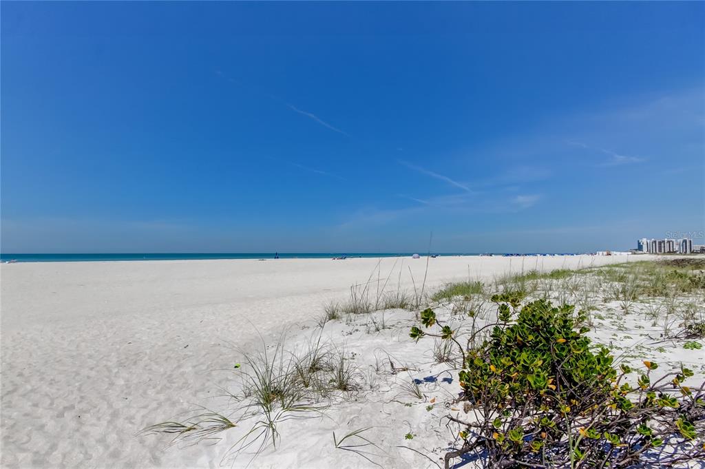 A wide, sandy beach stretches toward the ocean under a clear blue sky — 1200 GULF BOULEVARD UNIT 101, CLEARWATER BEACH, FL