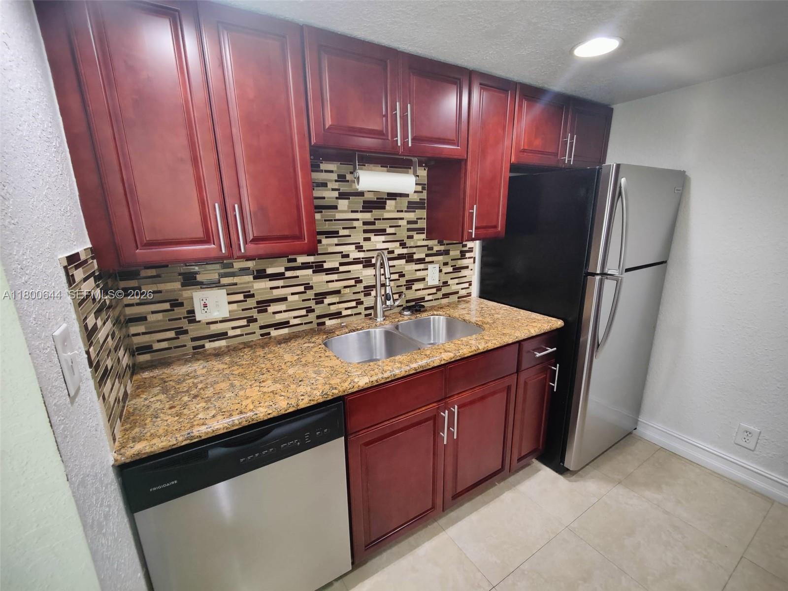 A kitchen features cherry wood cabinets, granite countertops, stainless steel appliances, and a tiled backsplash — 616 Executive Center Dr # 107, West Palm Beach FL 33401, WEST PALM BEACH, FL