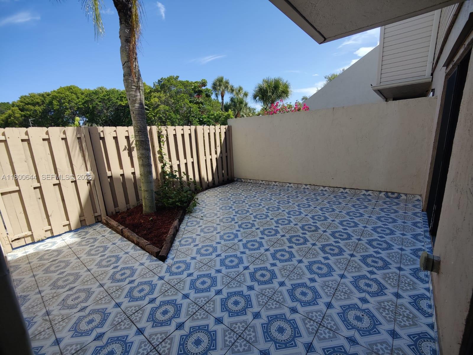 A tiled patio features a small garden bed with a palm tree and wooden fencing — 616 Executive Center Dr # 107, West Palm Beach FL 33401, WEST PALM BEACH, FL