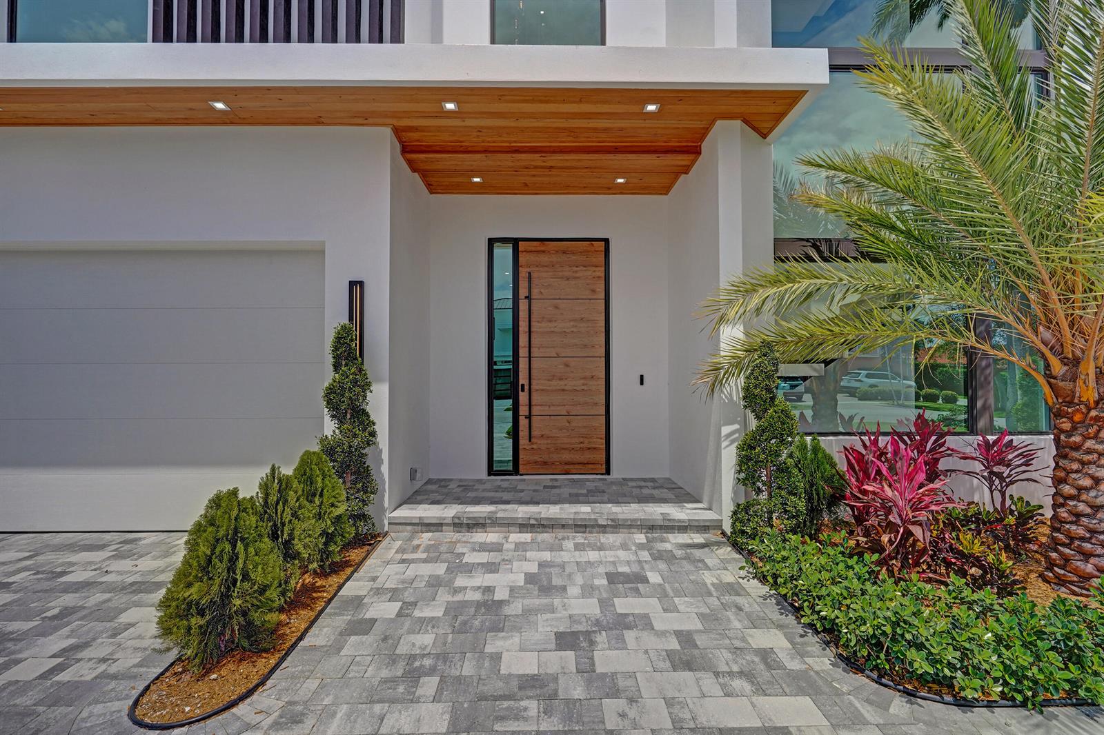 A modern home exterior features a wood-paneled front door, a paved walkway, and landscaping — 365 NE 3rd Street, Boca Raton FL 33432, BOCA RATON, FL