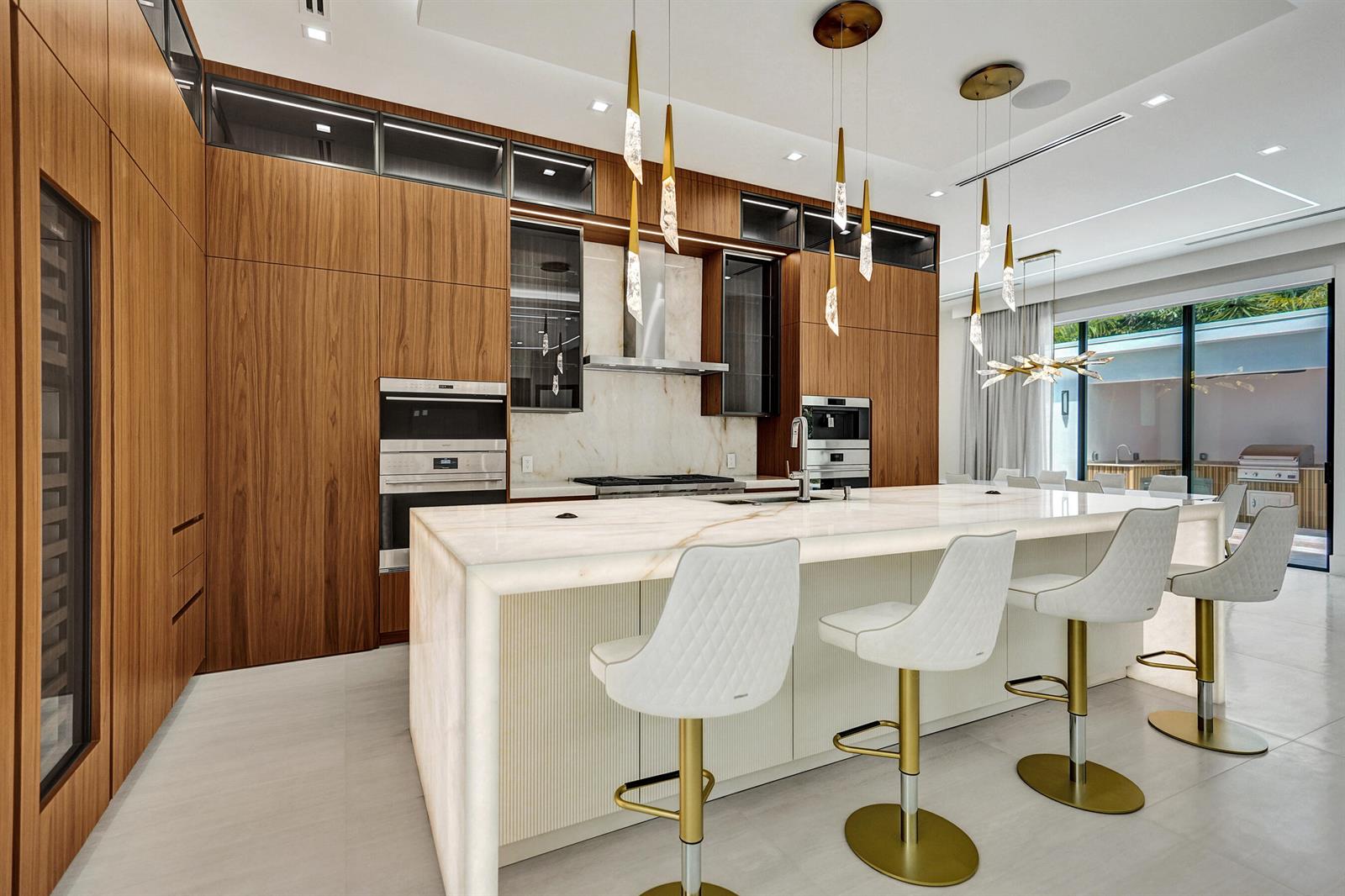 A modern kitchen features wood cabinetry, a large stone island, and white bar stools — 365 NE 3rd Street, Boca Raton FL 33432, BOCA RATON, FL