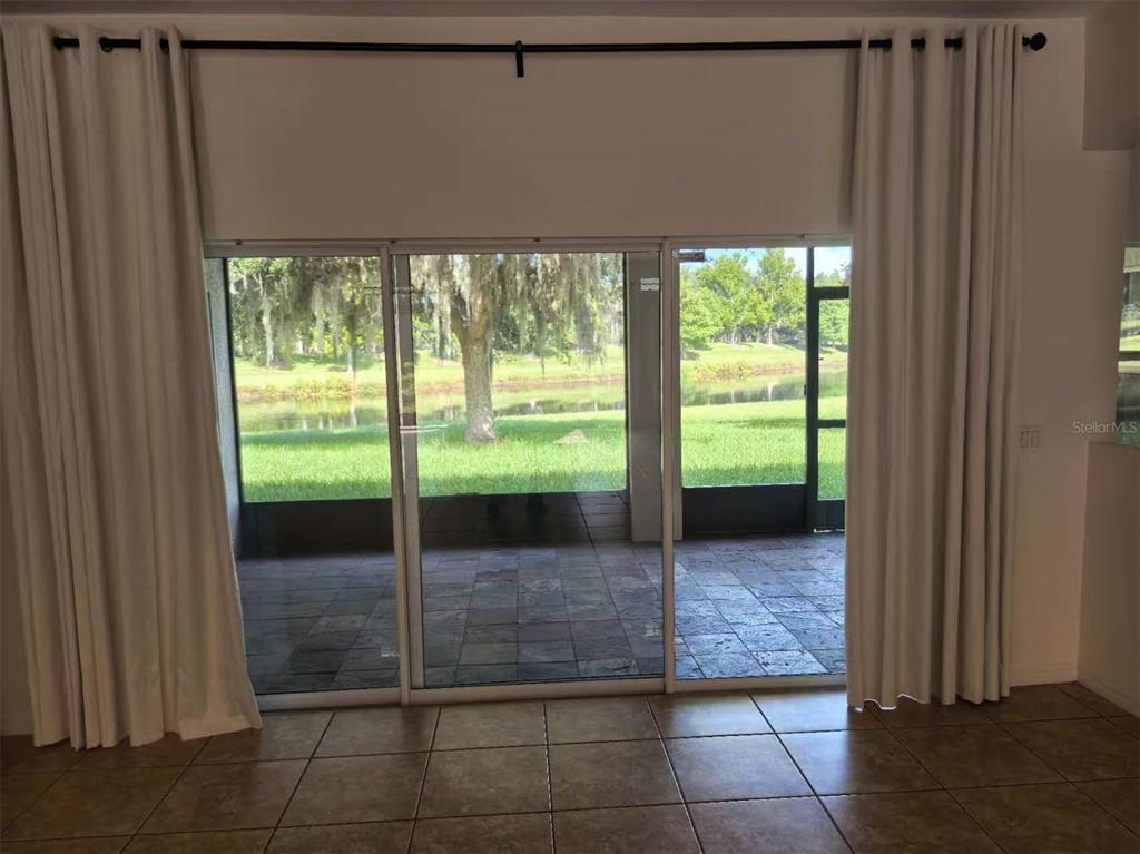A room with tile flooring features sliding glass doors opening to a screened patio and pond — 3520 SHOREWOOD DRIVE, KISSIMMEE, FL