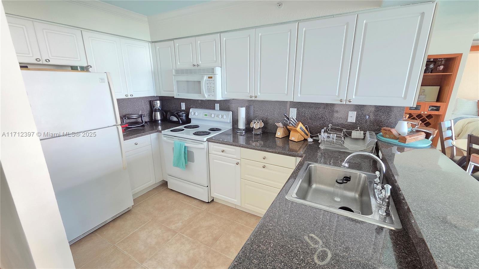 A kitchen features white cabinetry, dark granite countertops, a white refrigerator, and a stainless sink — 2501 S OCEAN DRIVE # 809, Hollywood FL 33019, HOLLYWOOD, FL