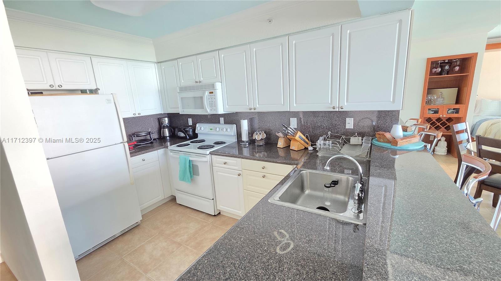 A kitchen features white cabinetry, dark granite countertops, and a stainless steel sink — 2501 S OCEAN DRIVE # 809, Hollywood FL 33019, HOLLYWOOD, FL
