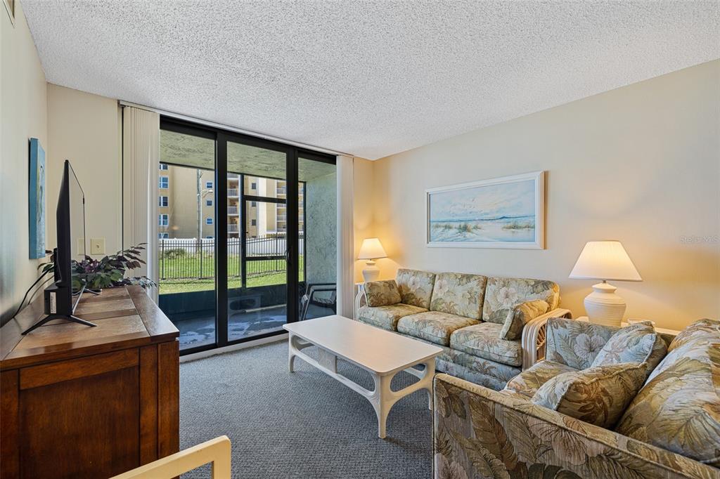 A living room features floral sofas, a white coffee table, and a sliding glass door — 3405 S ATLANTIC AVENUE UNIT 101, NEW SMYRNA BEACH, FL