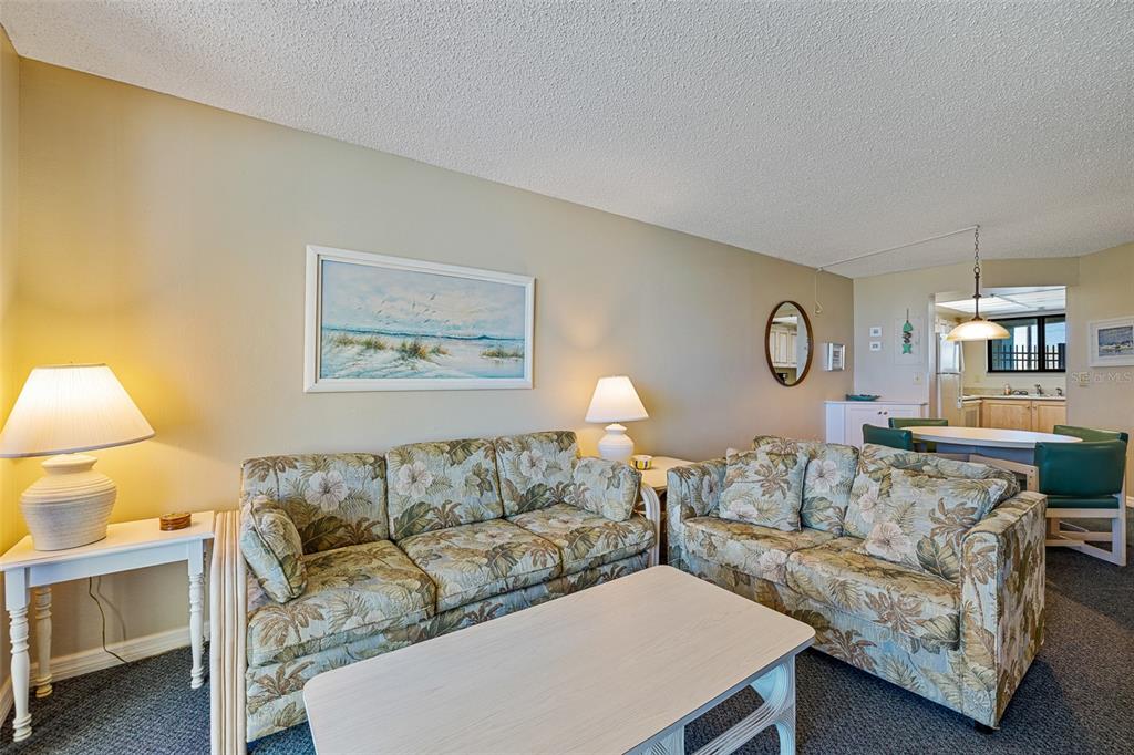 A living room features two floral sofas, a coffee table, and an adjacent dining area — 3405 S ATLANTIC AVENUE UNIT 101, NEW SMYRNA BEACH, FL