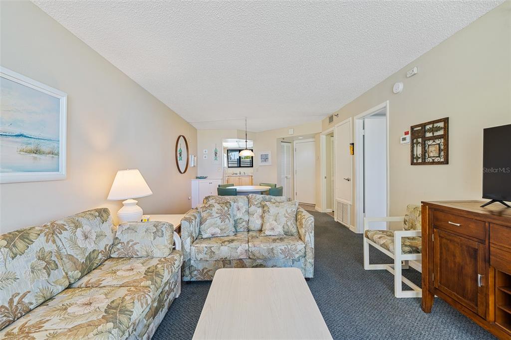 A living room features floral sofas, a coffee table, and a dining area beyond — 3405 S ATLANTIC AVENUE UNIT 101, NEW SMYRNA BEACH, FL