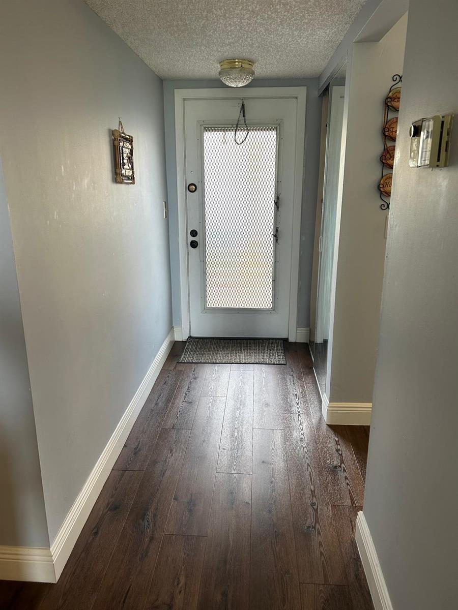 A hallway with dark wood-look flooring, light gray walls, and a white front door — 6670 Royal Palm Boulevard # 112k, Margate FL 33063, MARGATE, FL