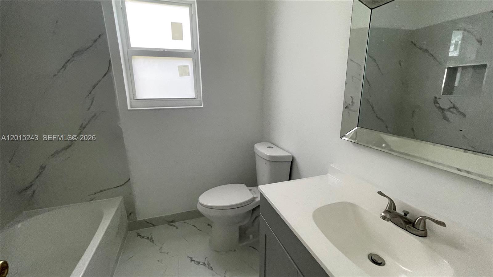 A bathroom features a white vanity, a toilet, and a bathtub with marble-patterned tile walls — 5210 NW 16th St, Lauderhill FL 33313, LAUDERHILL, FL