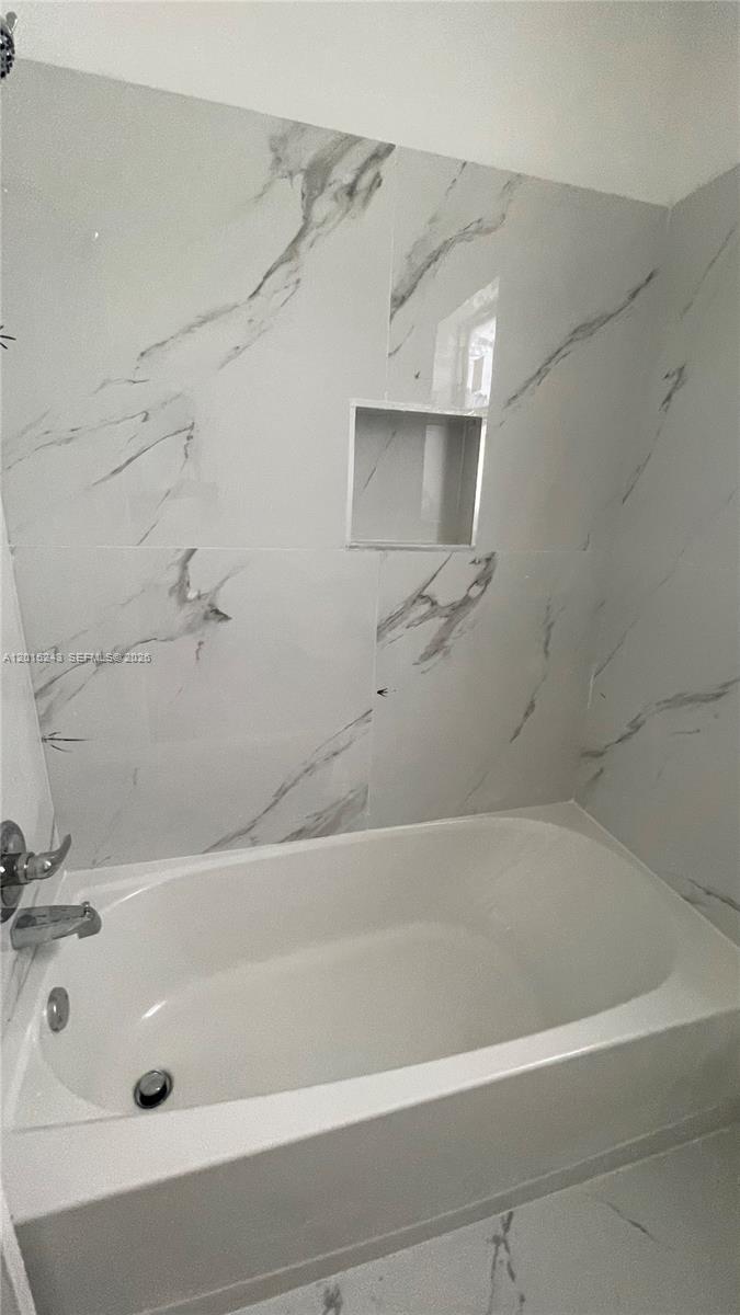 A white bathtub is set against a wall with large, white marble-patterned tiles — 5210 NW 16th St, Lauderhill FL 33313, LAUDERHILL, FL