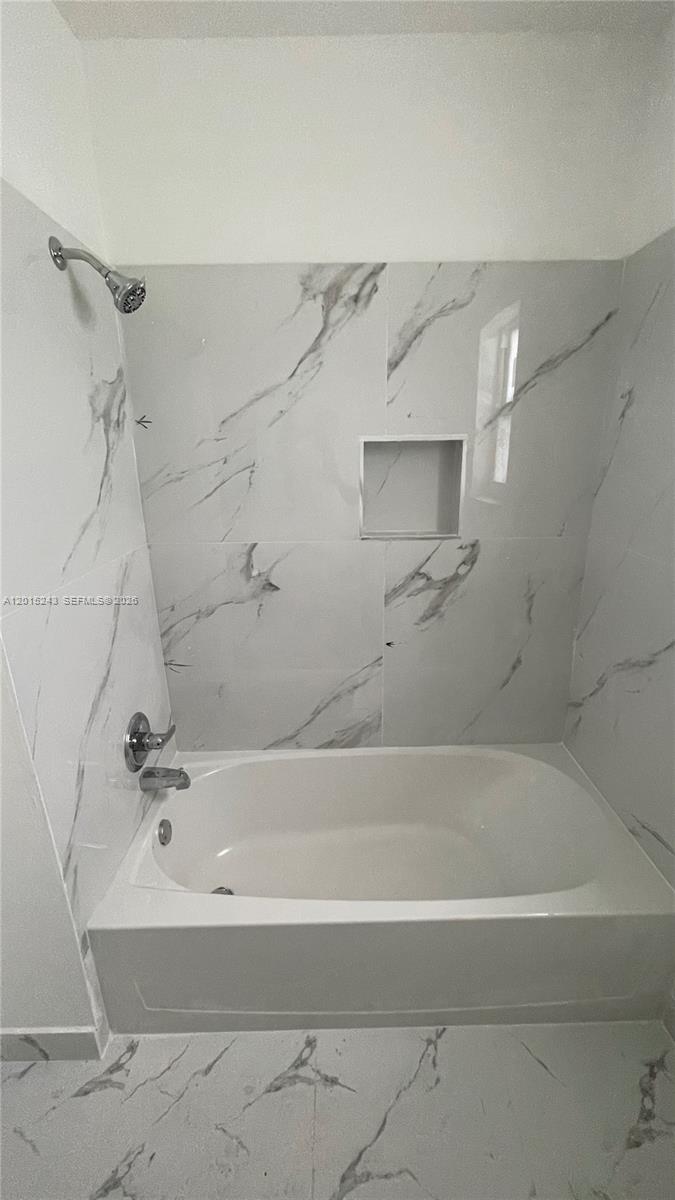 A bathroom features a white bathtub with a showerhead and marble-patterned tile walls — 5210 NW 16th St, Lauderhill FL 33313, LAUDERHILL, FL
