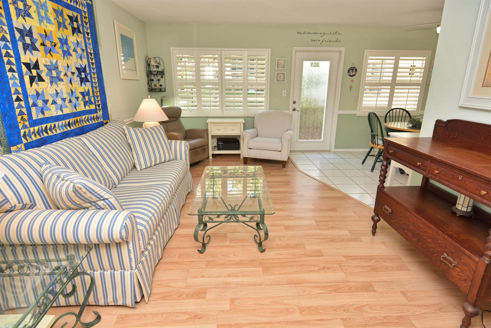 A living room features a striped sofa, glass coffee table, wood flooring, and a wall quilt — 1225 NW 21st Street # 203, Stuart FL 34994, STUART, FL