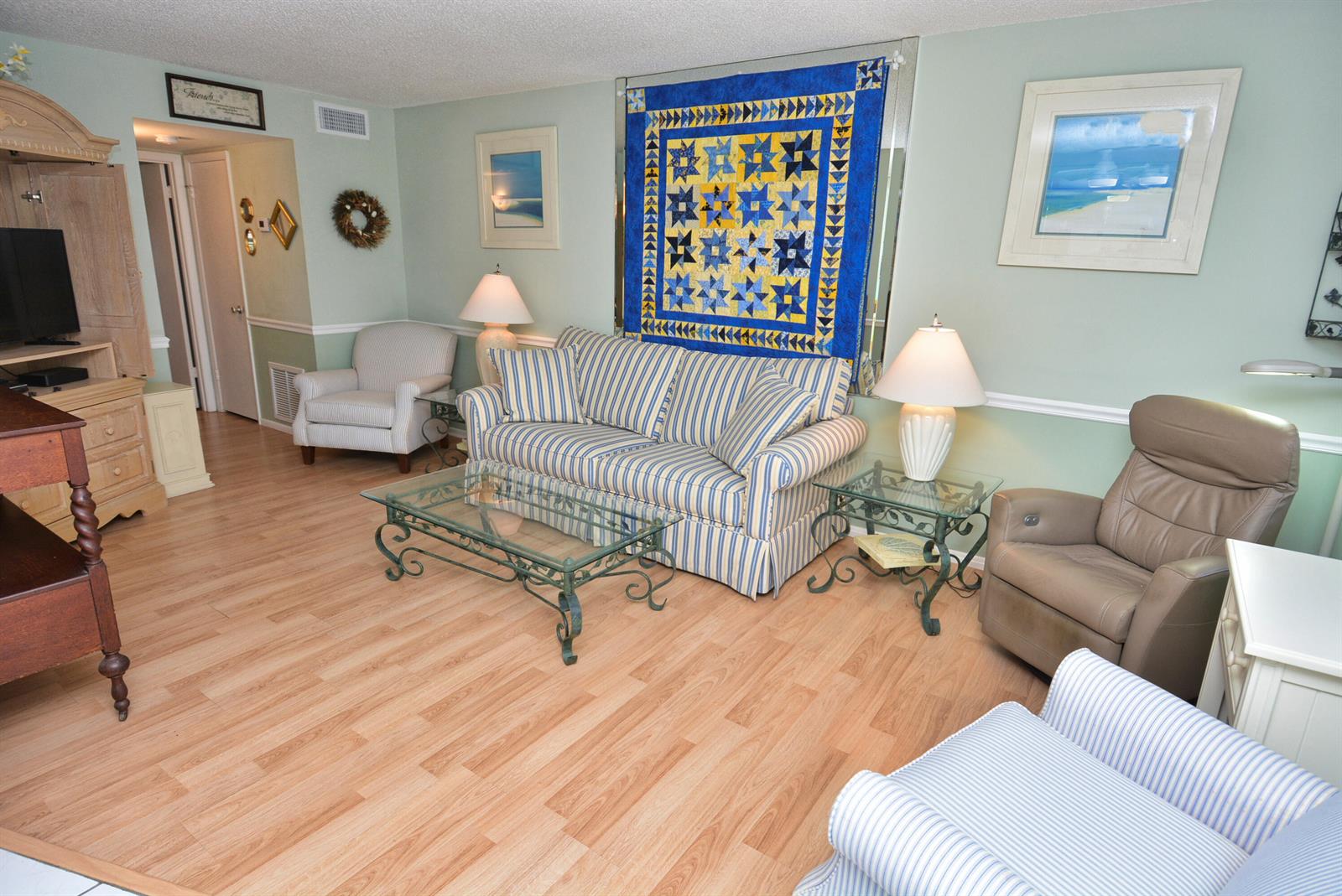 A living room features a striped sofa, a glass coffee table, and a wall-mounted quilt — 1225 NW 21st Street # 203, Stuart FL 34994, STUART, FL