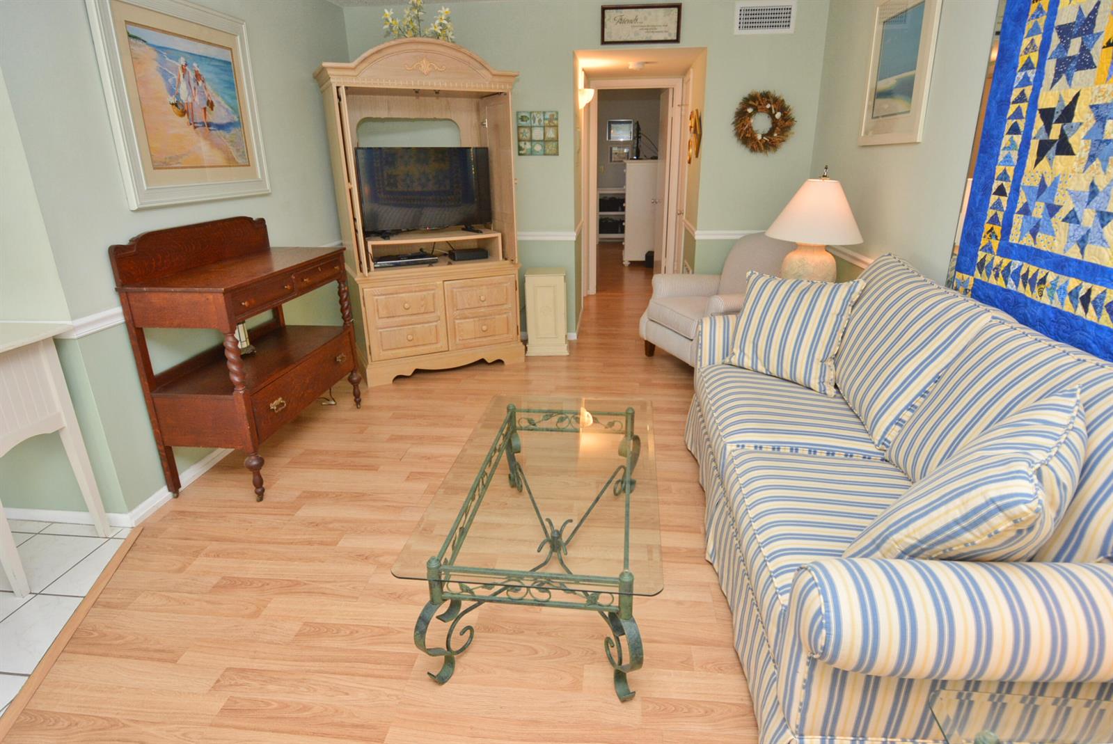 A living room features a striped sofa, glass coffee table, wooden hutch, and light flooring — 1225 NW 21st Street # 203, Stuart FL 34994, STUART, FL