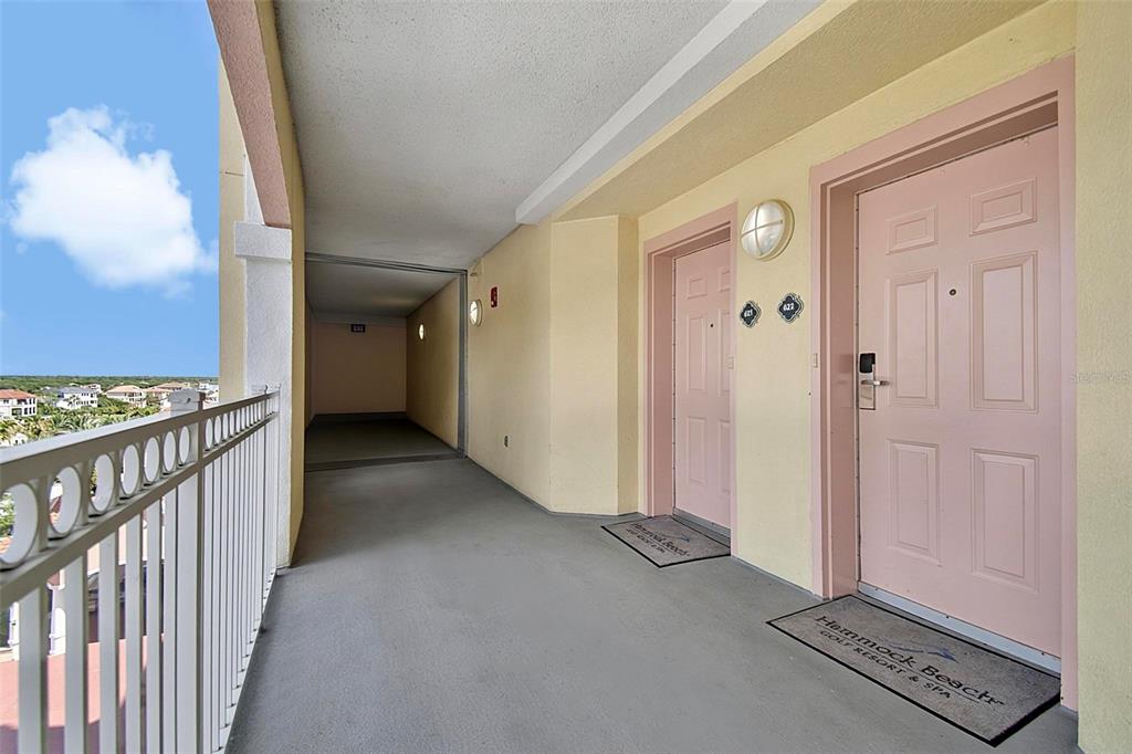 An outdoor hallway features two pink doors with welcome mats and a white metal railing — 200 OCEAN CREST DRIVE UNIT 622, PALM COAST, FL