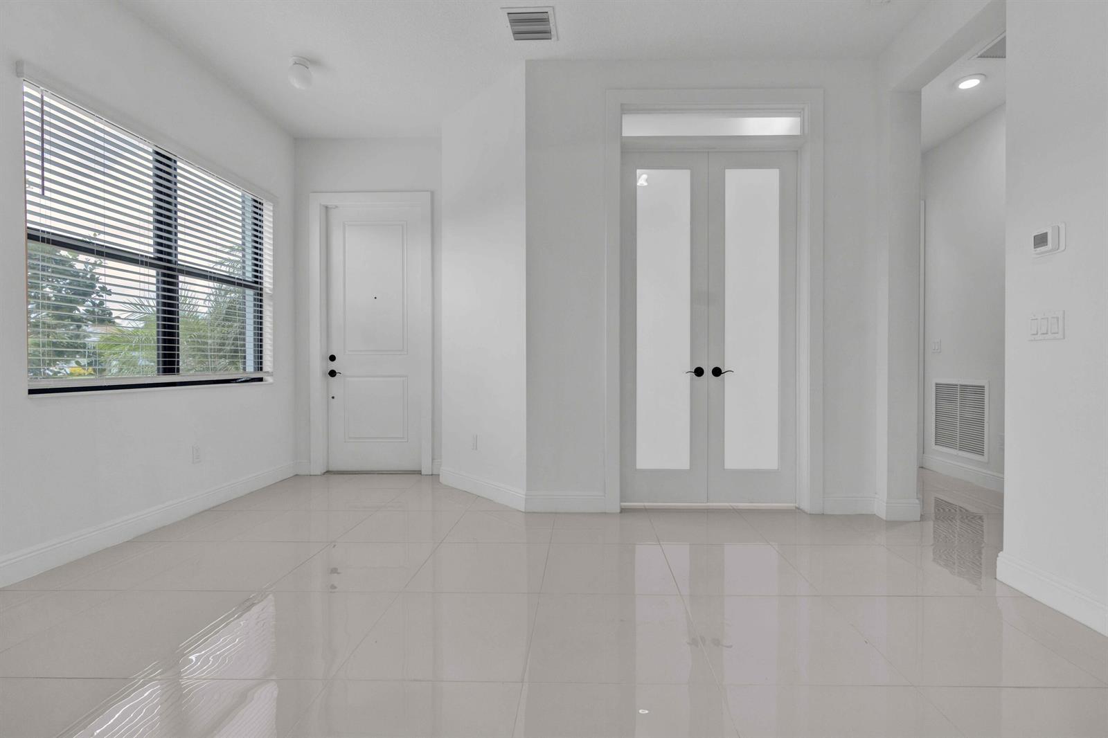 An empty room with white walls, glossy tile floors, a window with blinds, and two doors — 5501 Santa Rosa Lane, Westlake FL 33470, WESTLAKE, FL