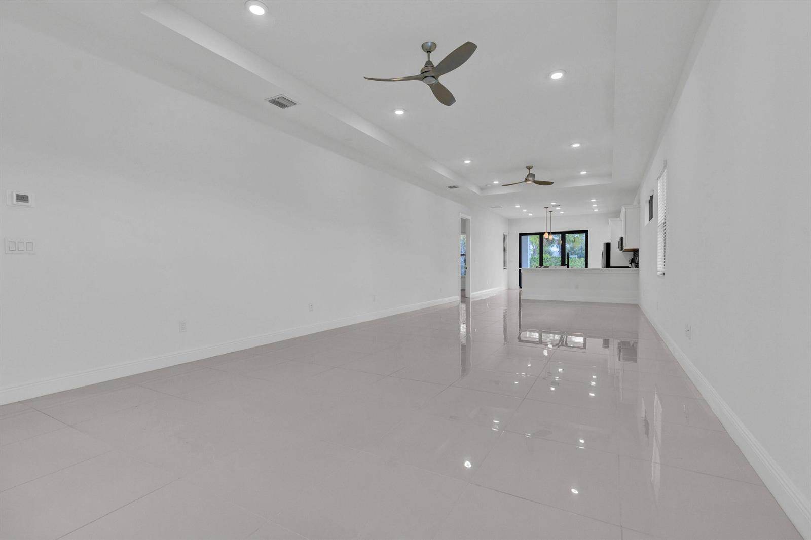 A spacious, minimalist living room with white walls, glossy tile floors, and two ceiling fans — 5501 Santa Rosa Lane, Westlake FL 33470, WESTLAKE, FL